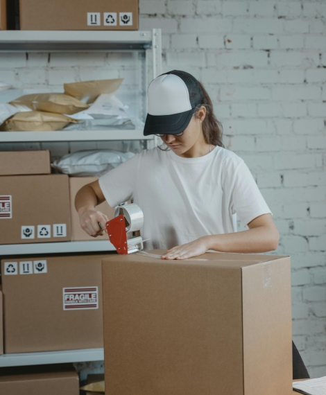 Young female worker sealing cardboard boxes in an indoor warehouse setting.